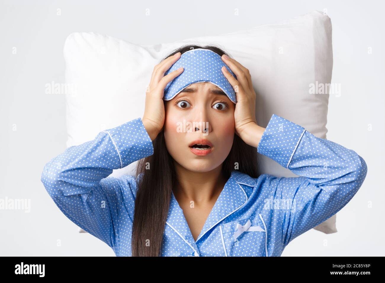 Closeup shot of panicking asian cute girl lying in bed on pillow in