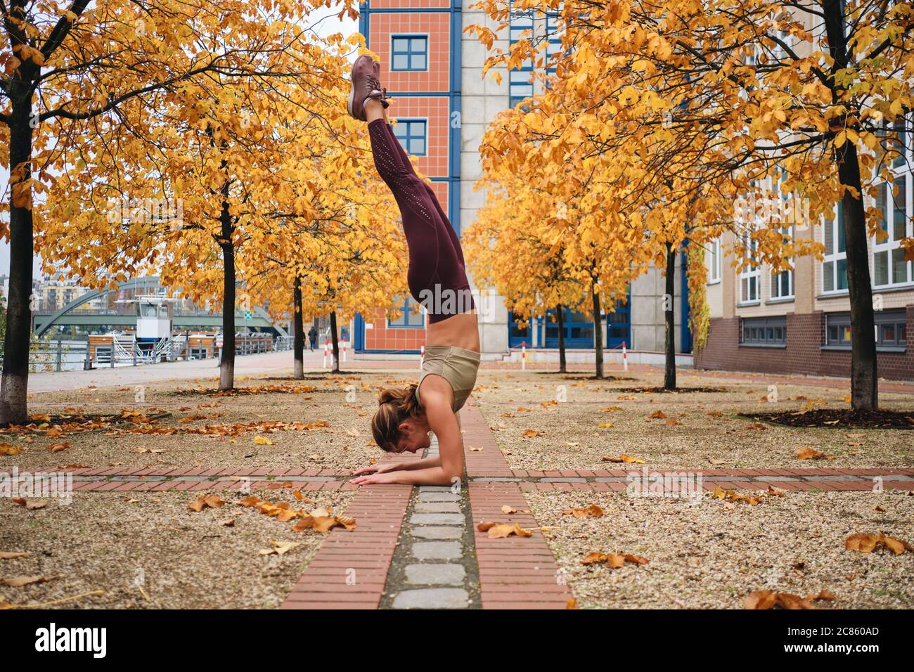 Side view of pretty girl in sportswear standing on hands during yoga practice on city street Stock Photo