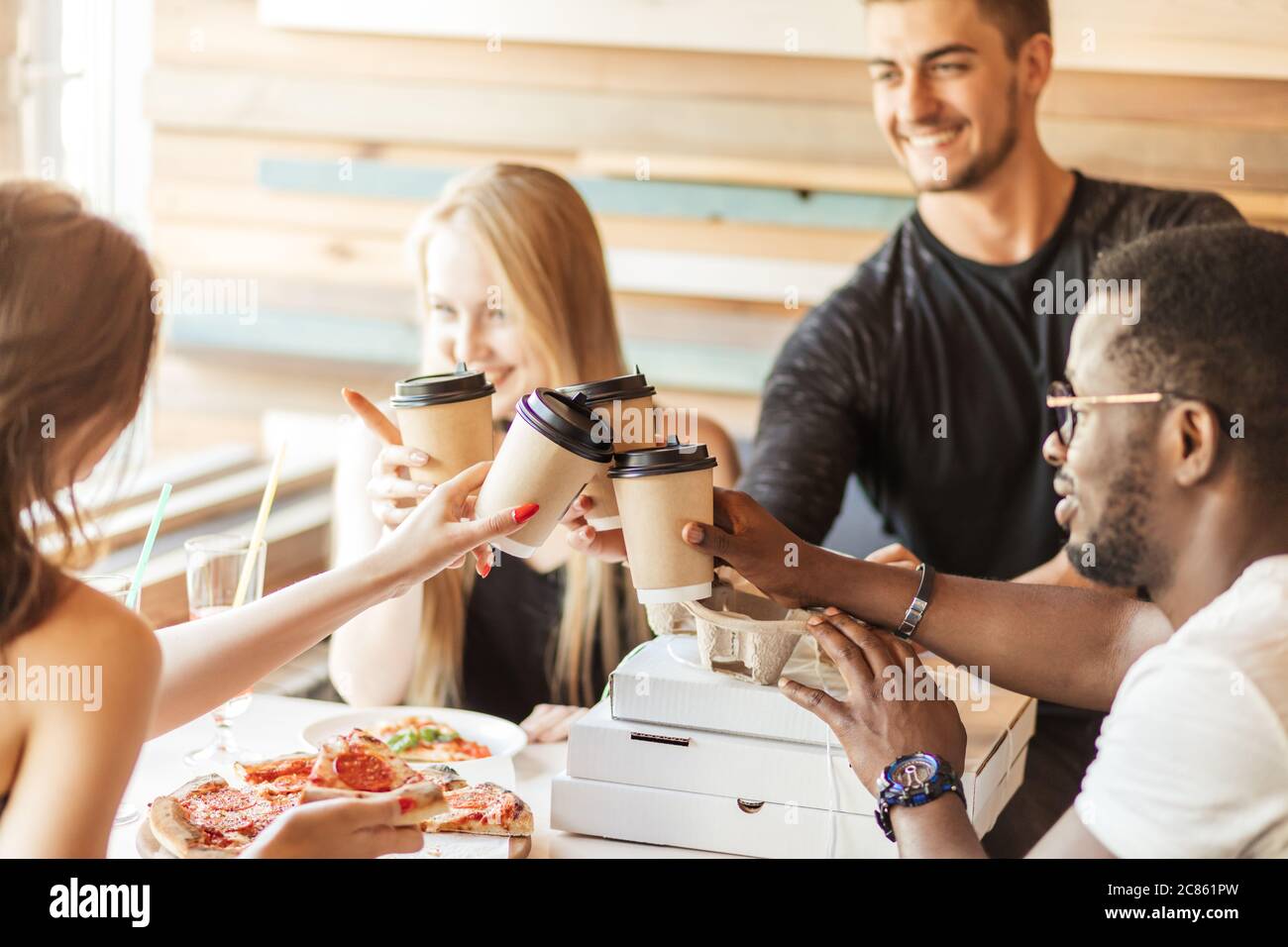 Group of young multiracial friends hanging out at a coffee shop. Young men and women meeting in a cafe having fun, eating pizza and drinking coffee Stock Photo