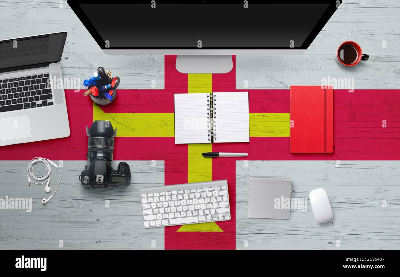 Guernsey flag background with headphone,camera, notebook and mouse on national office desk table