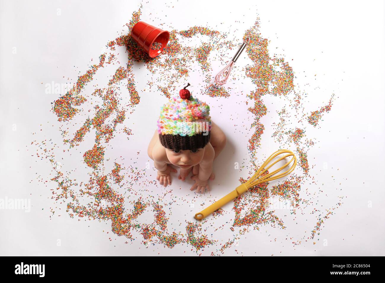 Baby wearing a cupcake hat among whiskers and sprinkles. Stock Photo