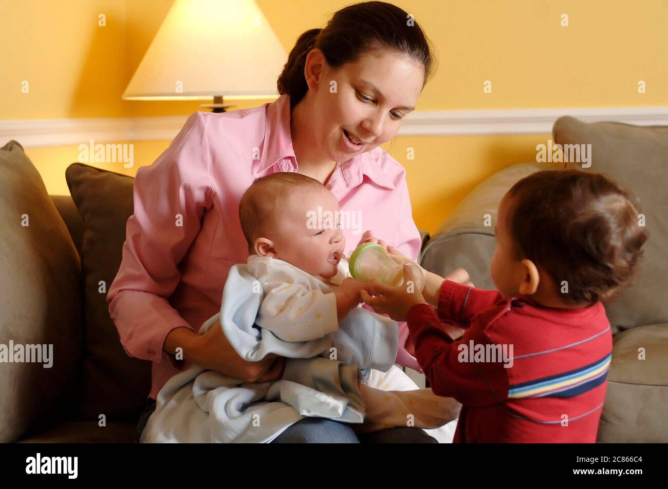 Austin, Texas USA, January 2006: Hispanic mom, early 30's, holds her three-month old newborn while 22-month old brother tries feeding with a bottle at home.  MR   ©Bob Daemmrich Stock Photo