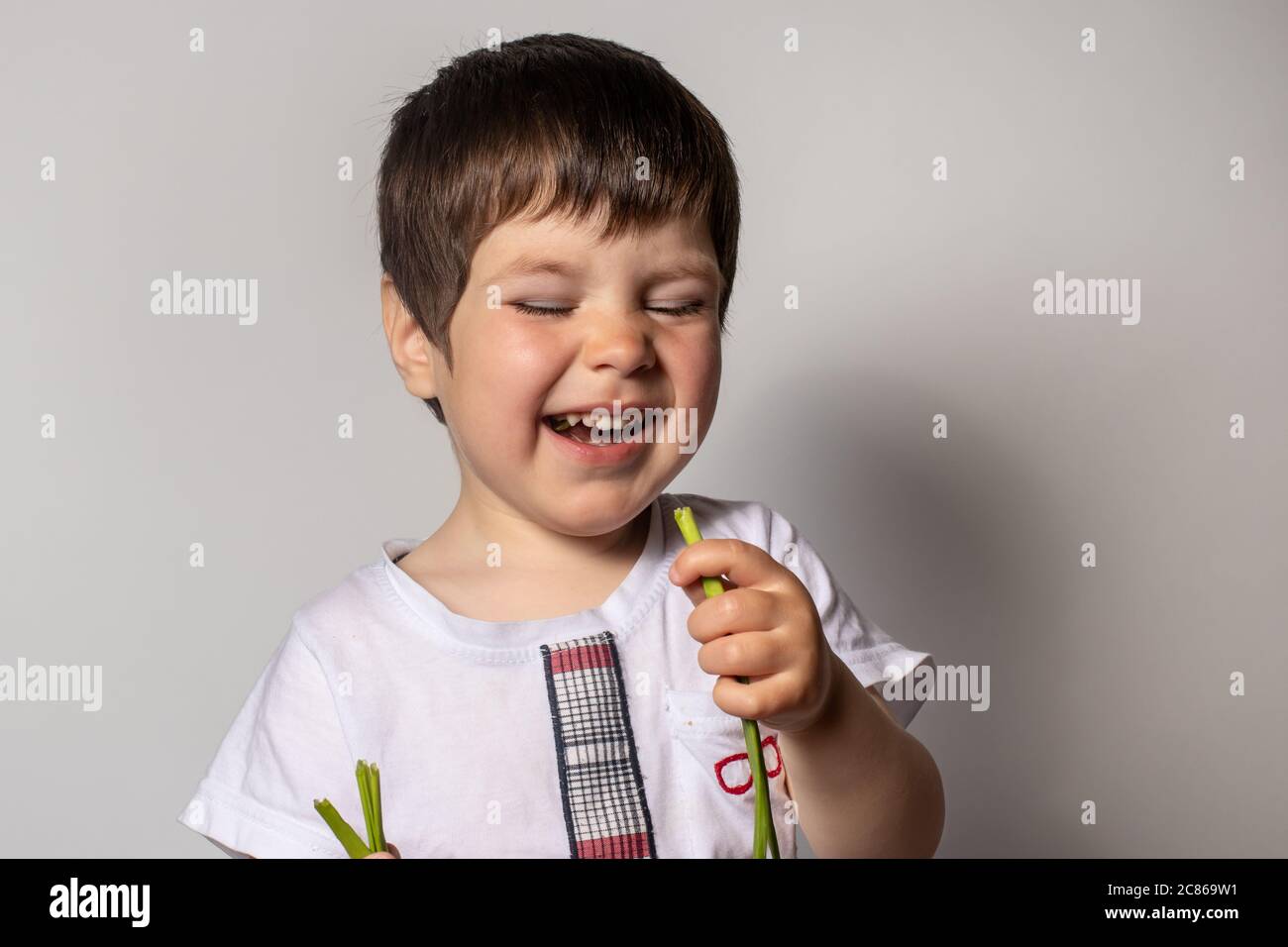 Little boy eats green onion and laughs. Proper nutrition of children