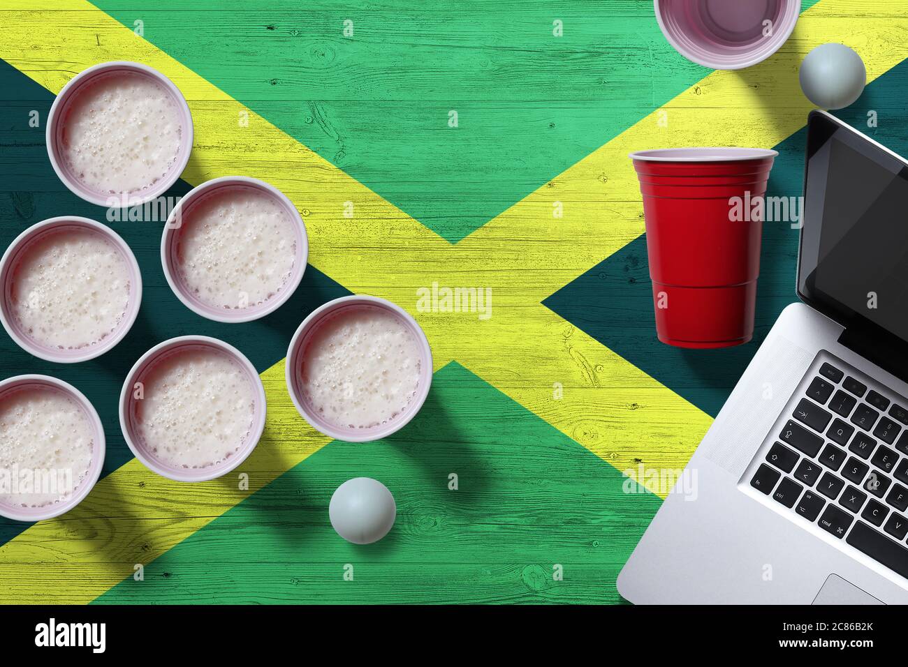 Jamaica flag concept with plastic beer pong cups and laptop on national wooden table, top view