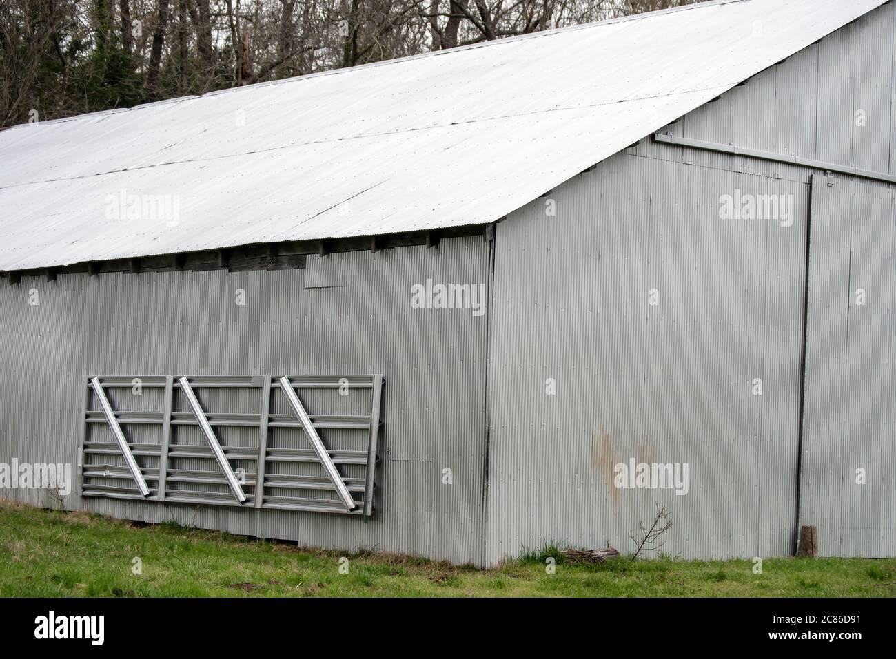 A tin barn shines brightly in the sunlight on a farm in Missouri. A portable metal gate hangs on the side of the barn ready for use when needed. Stock Photo