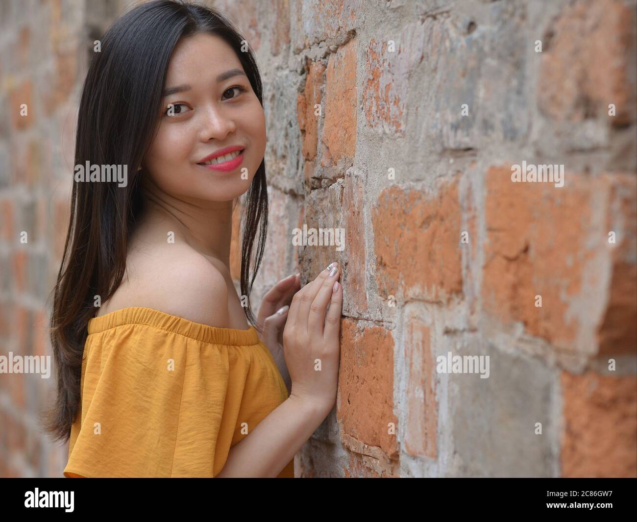 Beautiful Vietnamese girl wears a yellow off-shoulder top and poses for the camera. Stock Photo