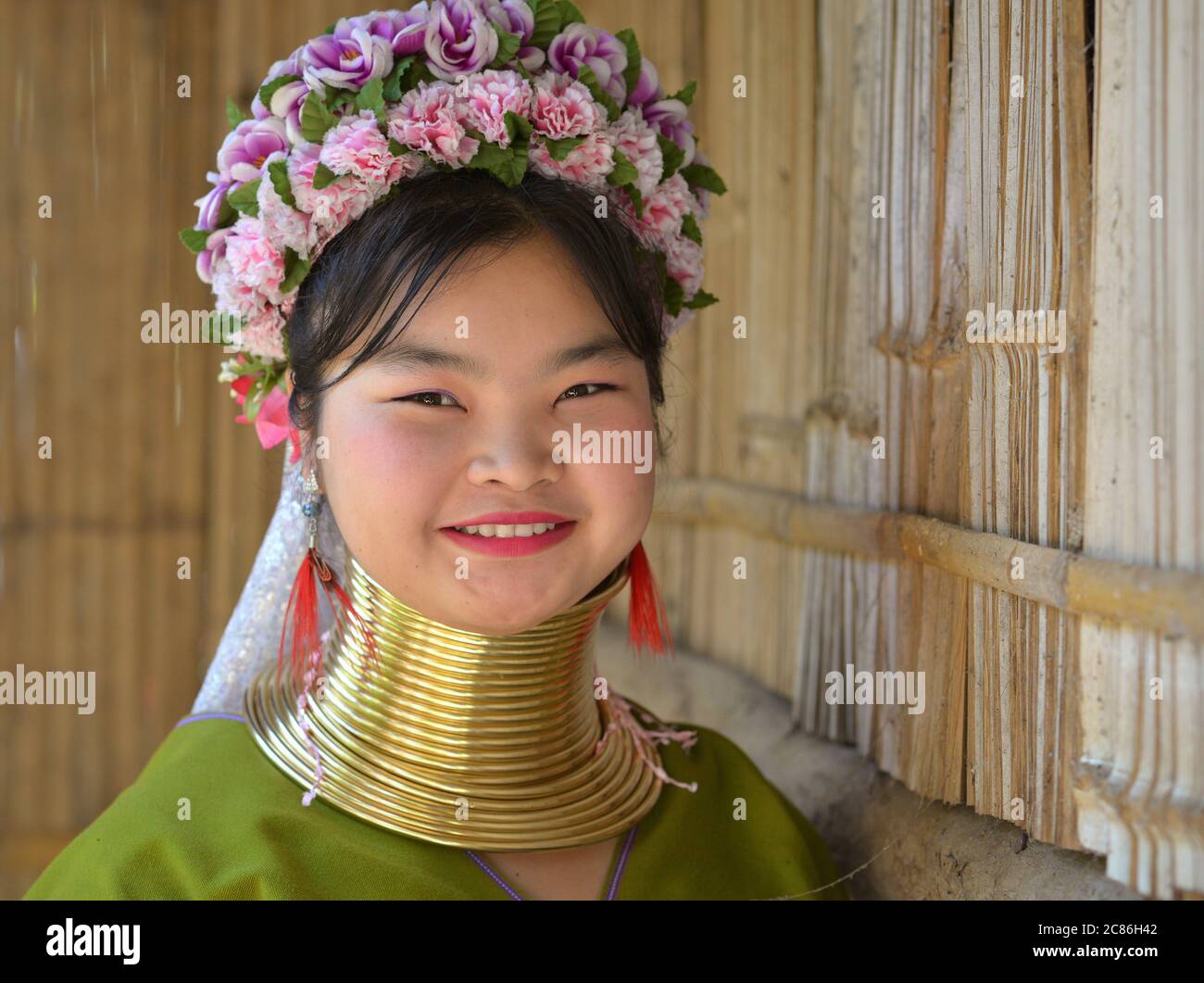 Chubby Thai/Burmese long-neck Kayan salesgirl (“giraffe woman”) with tribal Padaung brass neck rings/coils smiles for the camera. Stock Photo