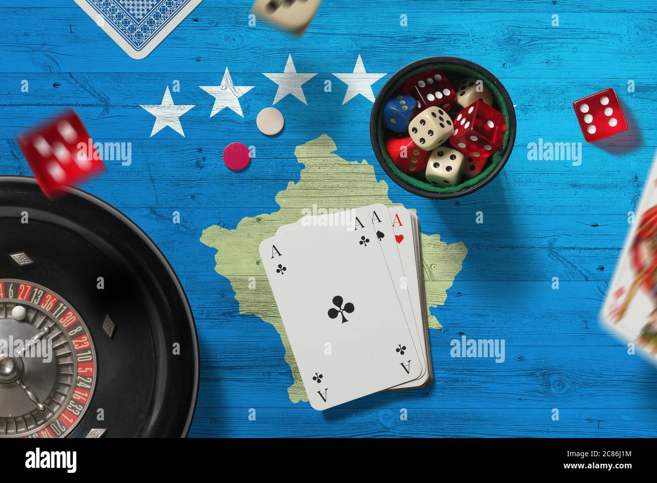 Kosovo casino theme. Aces in poker game, cards and chips on red table with national flag background. Gambling and betting. Stock Photo