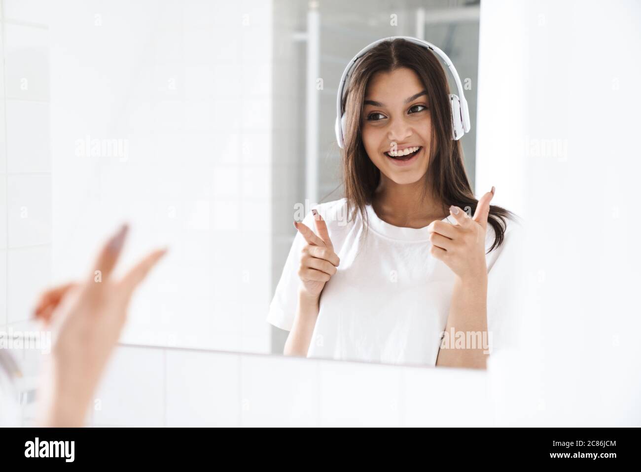 Photo of cheerful woman pointing finger at mirror while using wireless