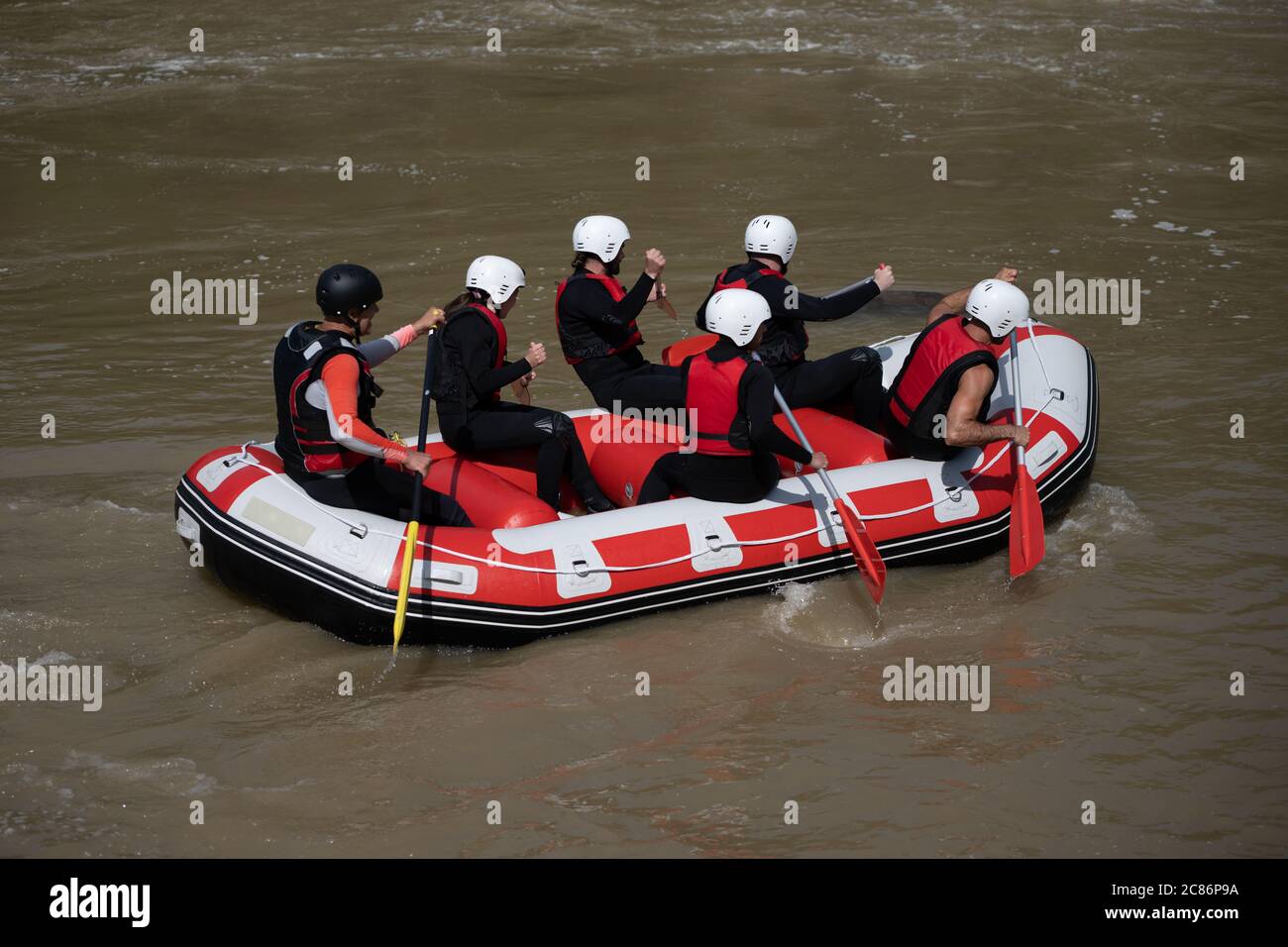 Rafting team members and instructor rowing in their boat down the murky river during a summer day. Practiging water sports can be good for your streng Stock Photo