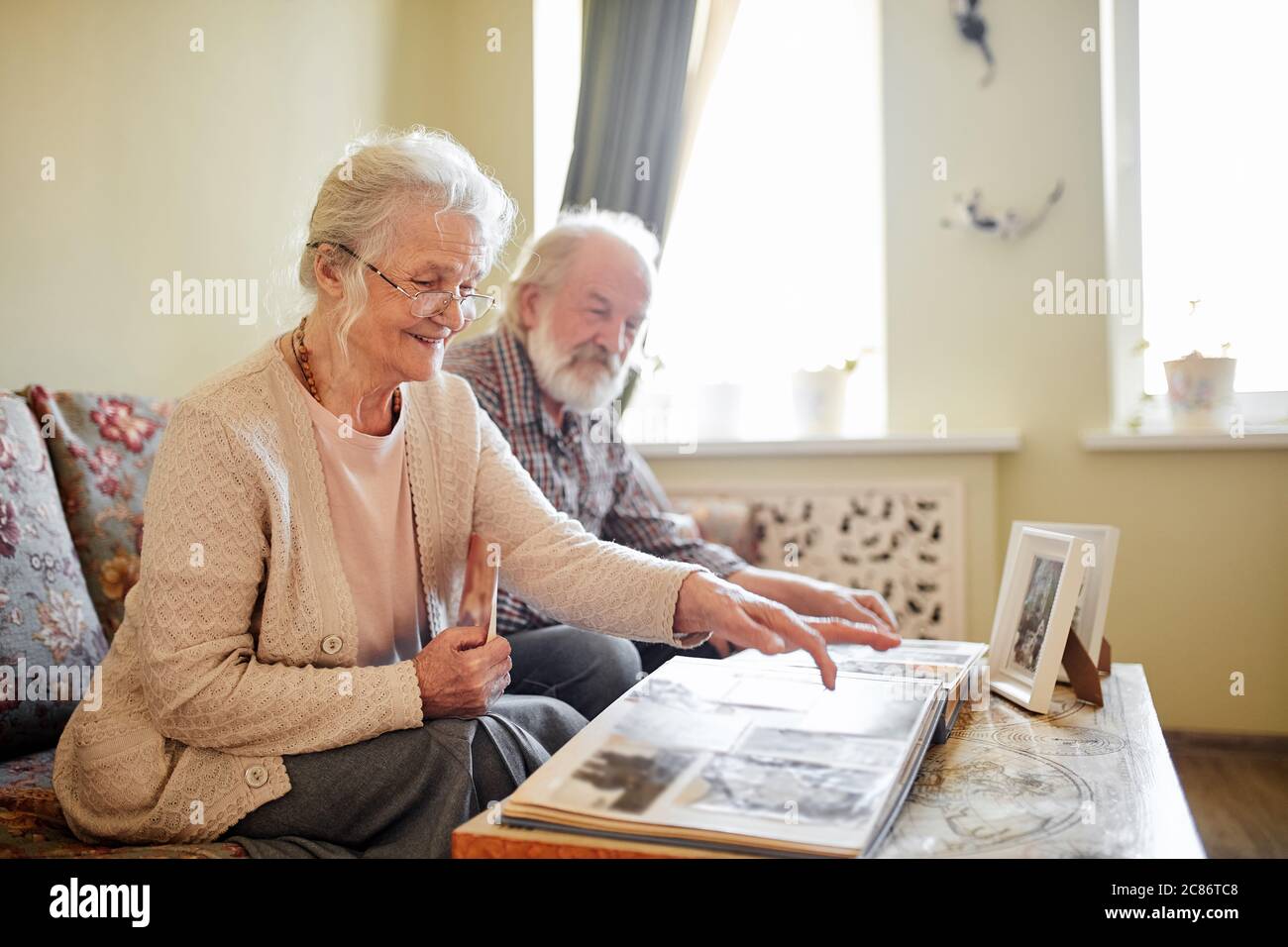 Senior couple looking at family photo album with vintage photos sitting ...