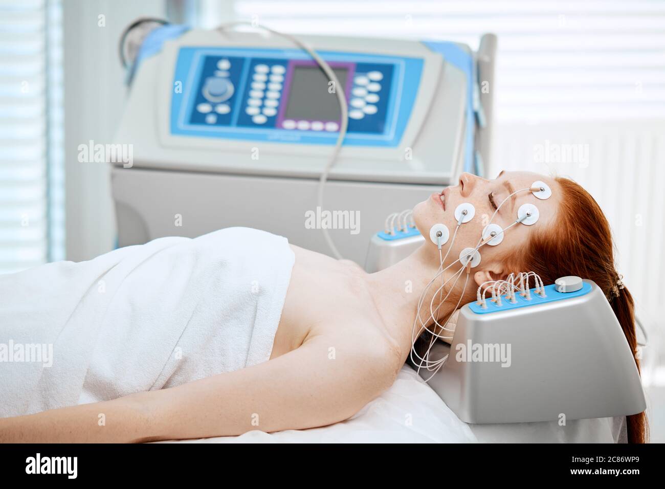 Young woman lying with electrodes on her face, receiving electric