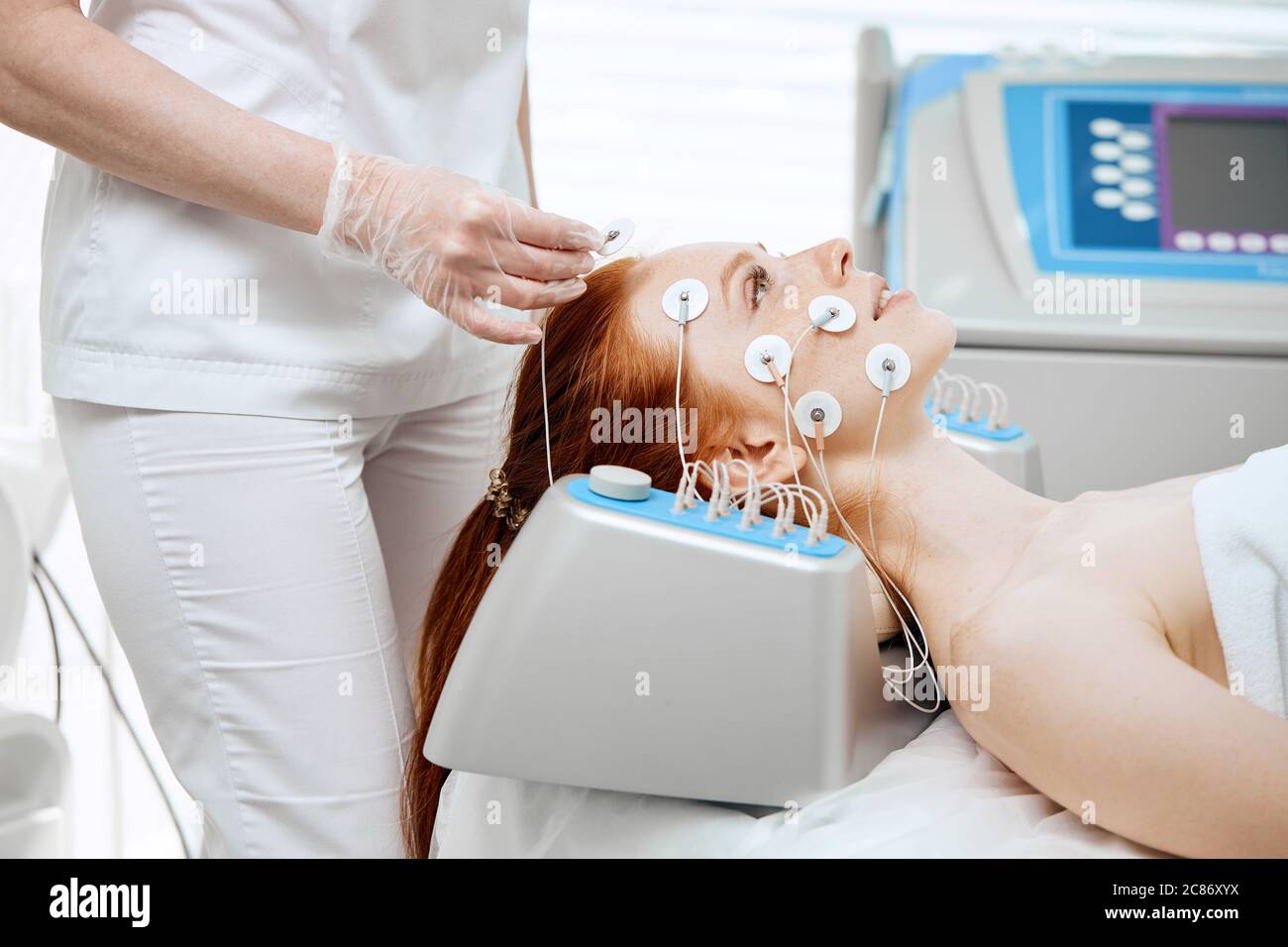 Young woman lying with electrodes on her face, receiving electric