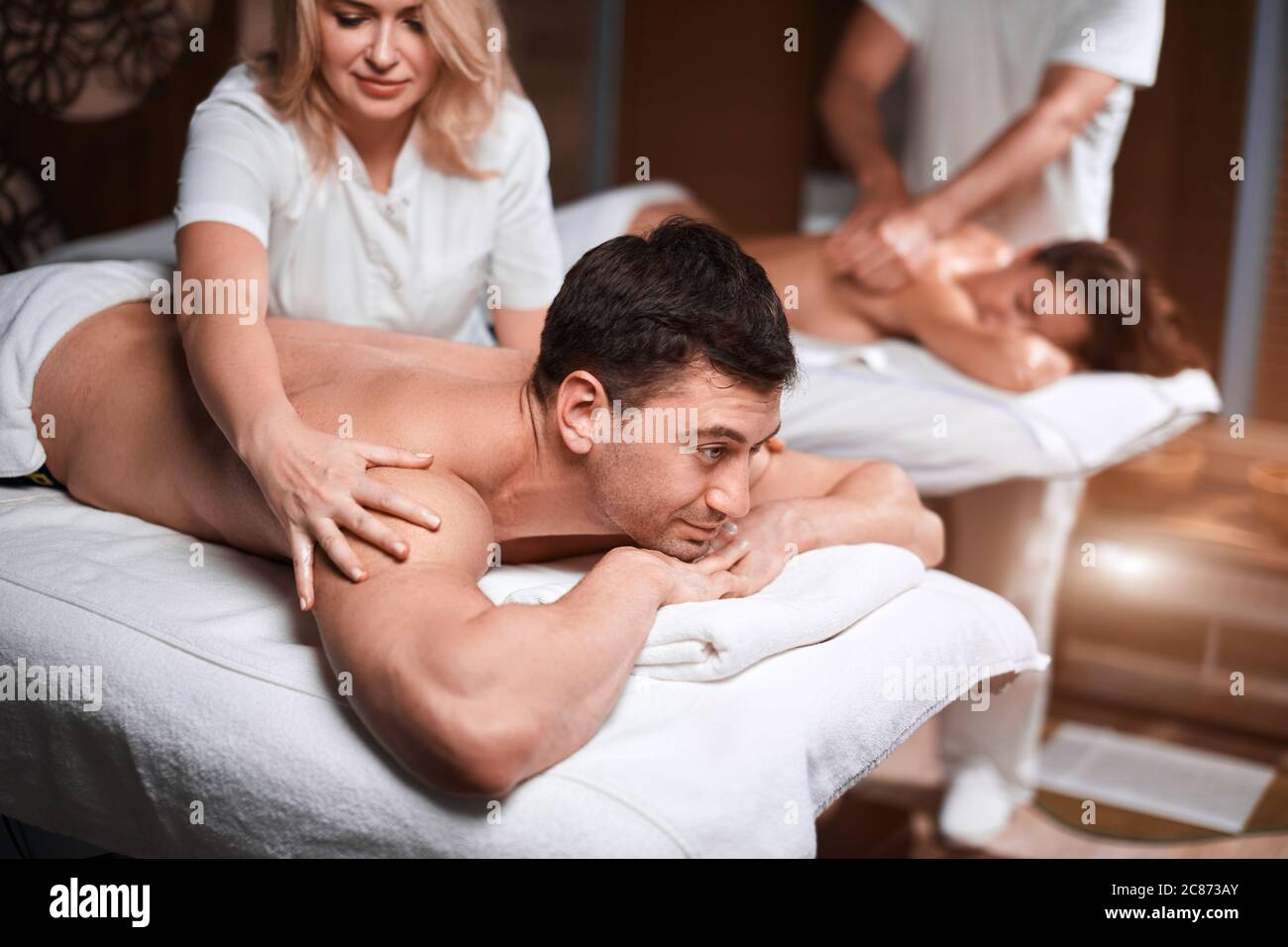 Handsome caucasian businessman and his beautiful wife treating themselves to a comforting back massage, a gentle relaxing massage at spa clinic. Stock Photo