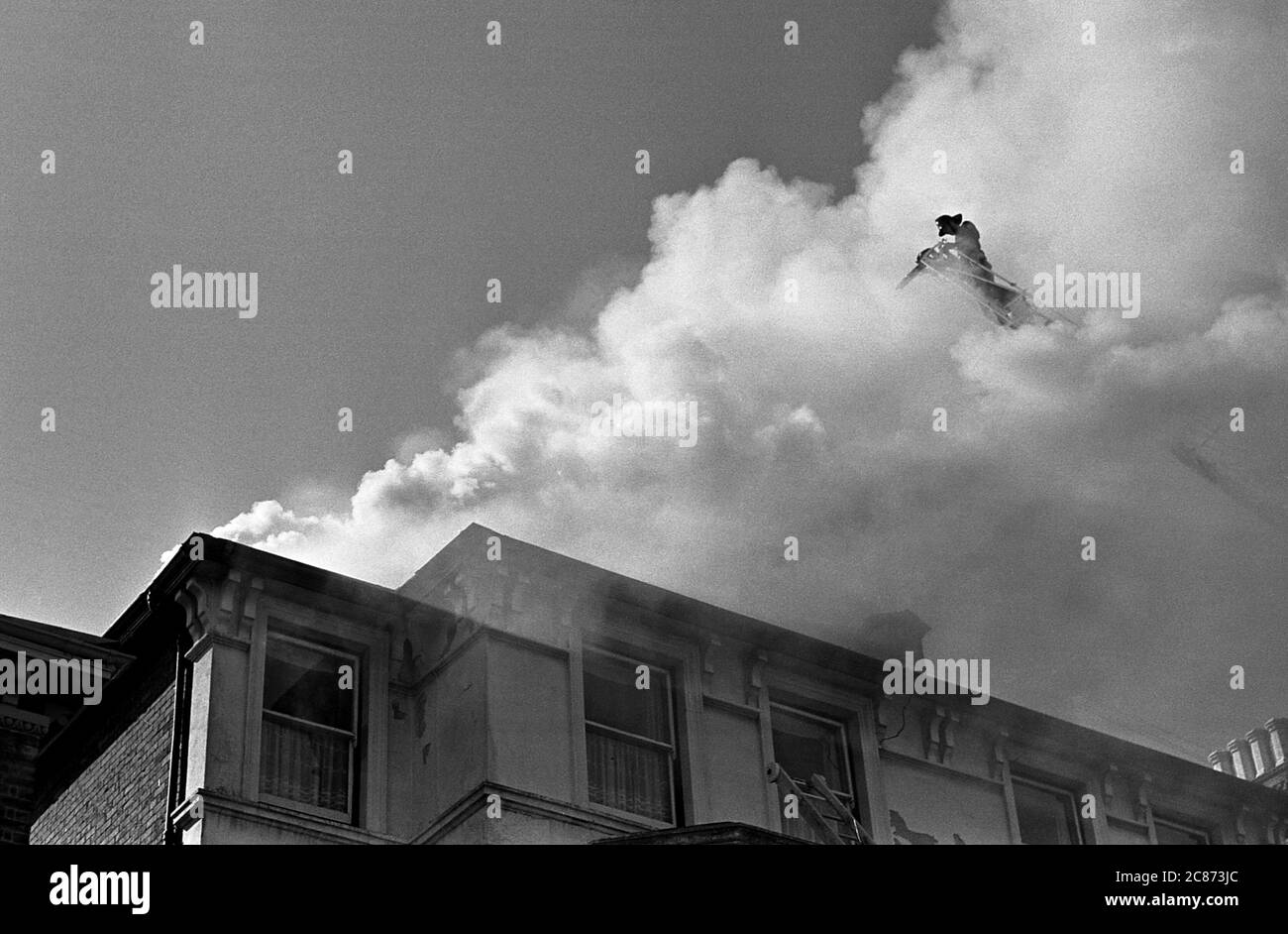 AJAXNETPHOTO. 7TH MARCH, 1969. SOUTHSEA, PORTSMOUTH, ENGLAND. - HOTEL FIRE - FIREMAN ATOP A TURNTABLE LADDER PARTLY OBSCURED BY SMOKE, POURS WATER INTO THE BLAZING ROOF OF THE HEREFORD HOTEL IN KENT ROAD. OCCUPANTS OF THE HOTEL WERE SAFELY EVACUATED AND THERE WERE NO CASUALTIES.PHOTO:JONATHAN EASTLAND/AJAX REF:202206 24 Stock Photo