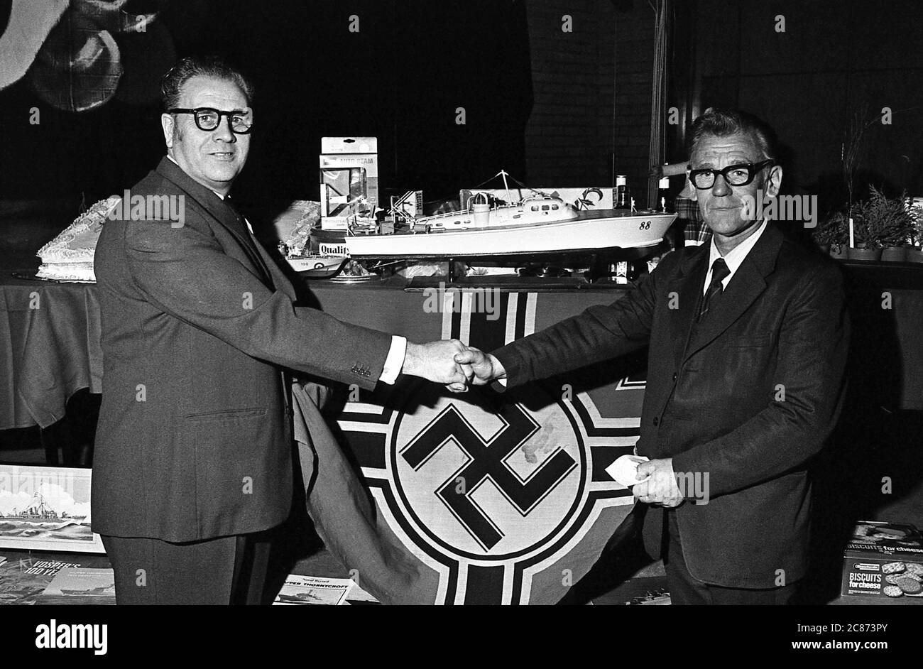 AJAXNETPHOTO. 29TH SEPTEMBER, 1974. PORTSMOUTH, ENGLAND. - INAUGURAL MEETING - (L-R) MR GORDON STEVENS OF DUNCAN ROAD, PORTSMOUTH, AND MR HAROLD PRINGLE OF MANCHESTER AT THE INAUGURAL MEETING OF THE COASTAL FORCES VETERANS ASSOCIATION AT THE VICTORY CLUB, HMS NELSON. BACKGROUND IS THE GERMAN KRIEGSMARINE BATTLE FLAG WHICH MR PRINGLE BROUGHT HOME AS A SOUVENIER WHEN THE GERMAN 'S' BOAT FLEET SURRENDERED AT ANCONA (ITALY) IN MAY 1945. MR PRINGLE WAS WITH THE 59TH MTB FLOTILLA. PHOTO:JONATHAN EASTLAND/AJAX REF:7527 7 Stock Photo