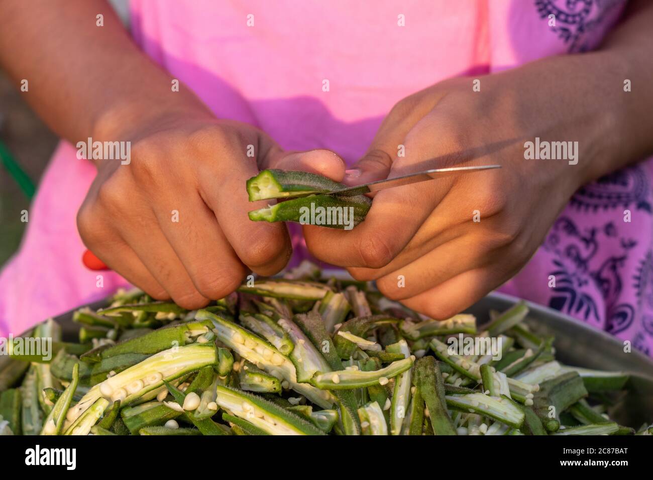 Young girl cutting okra lady finger with knife, preparing bhindi for cooking Stock Photo