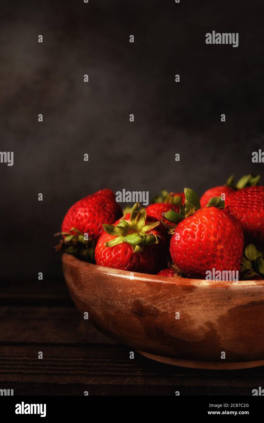 Still life of a bowl full of fresh picked strawberries on a wood table ...