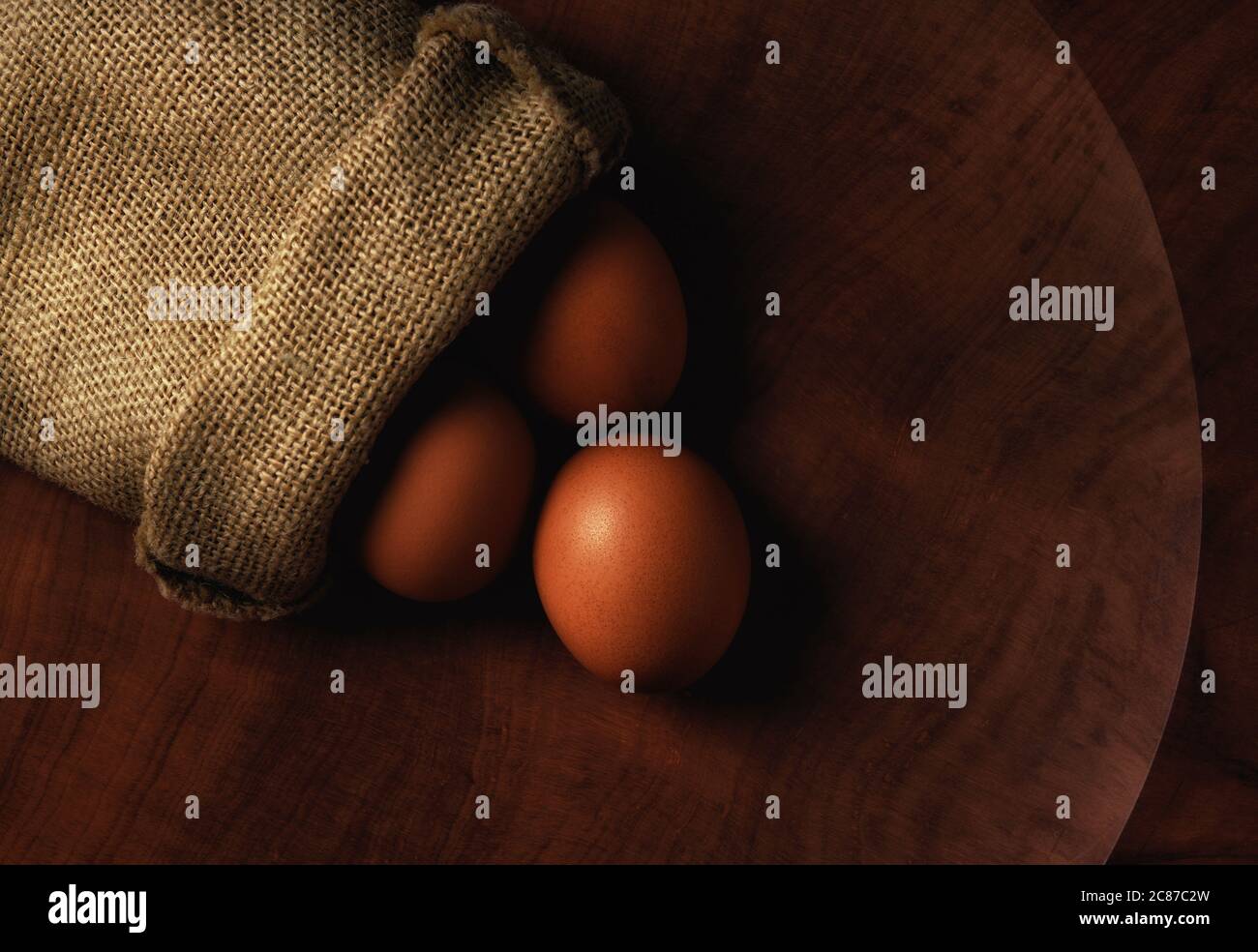 A burlap sack with eggs spilling out onto a large wooden platter. Flat ...