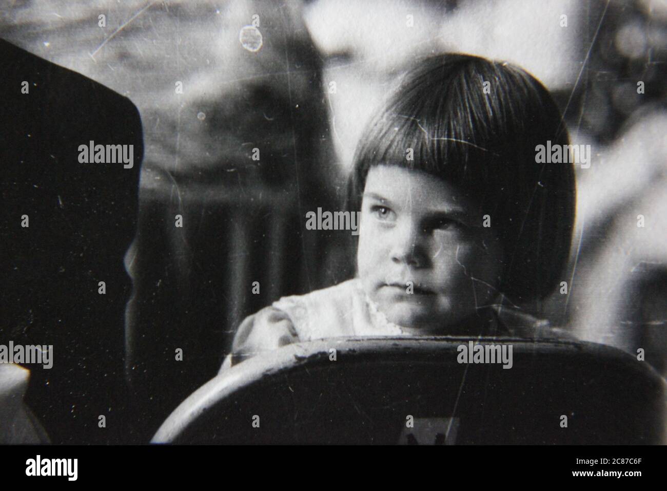 Fine 70s vintage black and white lifestyle photography of a beautiful three year old girl wearing a bowl cut by mom. Stock Photo