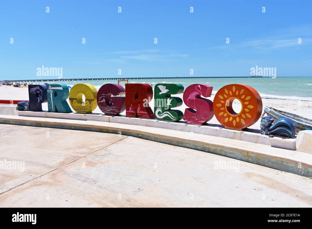 A large colourful sign for the city of Progreso along the promenade. The beach and sea can be seen behind and a pier crosses the whole image.  Mexico. Stock Photo