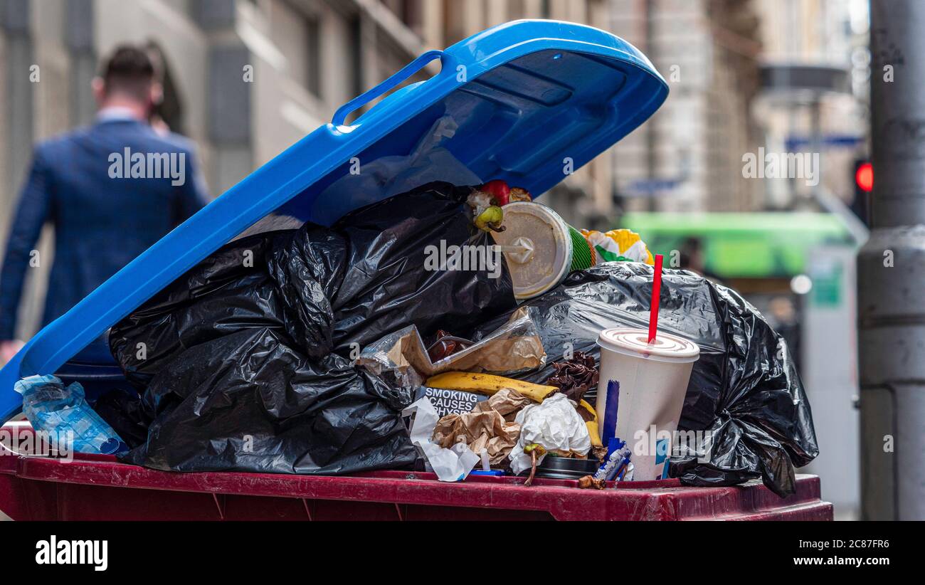 Urban rubbish bin overflowing in a populous city. Food scraps, plastic waste, single use bags. Shows recycling problems or issues, waste management. Stock Photo