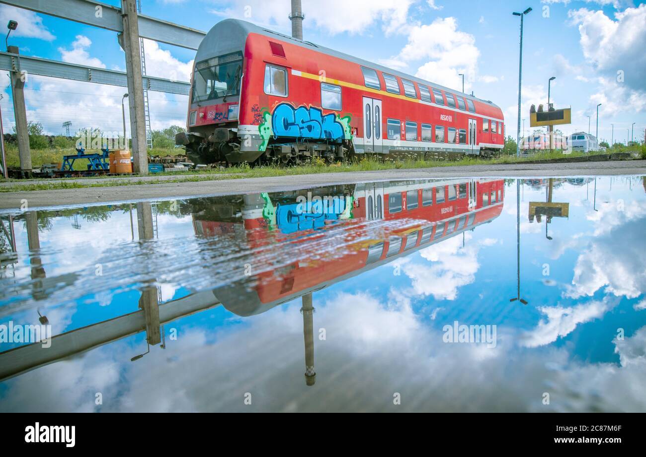 Mukran, Germany. 16th July, 2020. A double-decker passenger coach stands in front of the repair workshop of Baltic Port Services GmbH (BPS) and is reflected in a puddle. In the workshop, rail vehicles in GDR times were re-gauged from the 1520 millimetre wide Russian broad gauge to the standard track common in the rest of Europe. The workshop, which was taken over in 2014 by the current company Enon, based in Putlitz, Brandenburg, reconditions old locomotives and rail cars for use by private railway companies. Credit: Jens BŸttner/dpa-Zentralbild/dpa/Alamy Live News Stock Photo