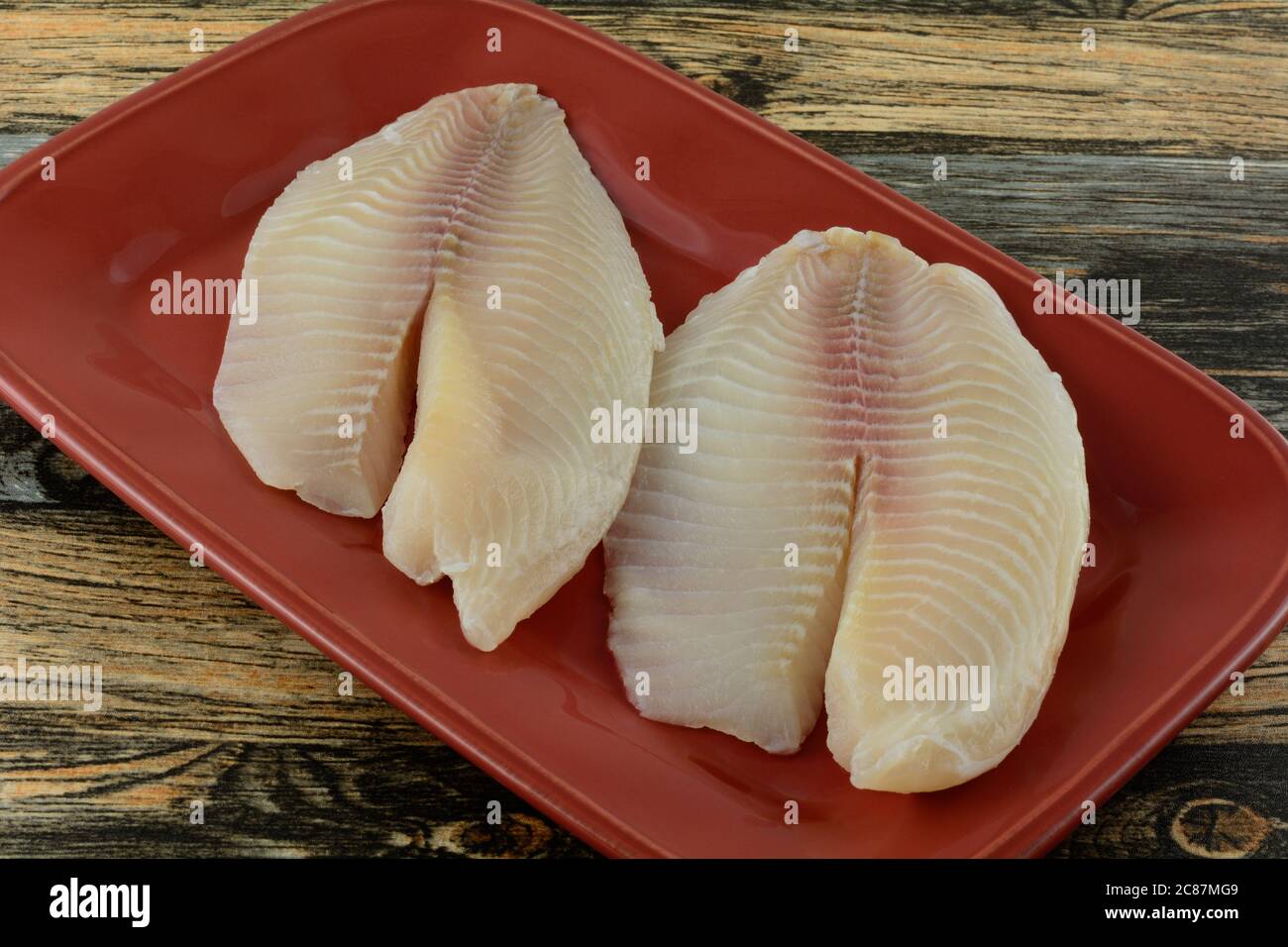 Fresh raw tilapia fish fillets on grilling ingredient platter in