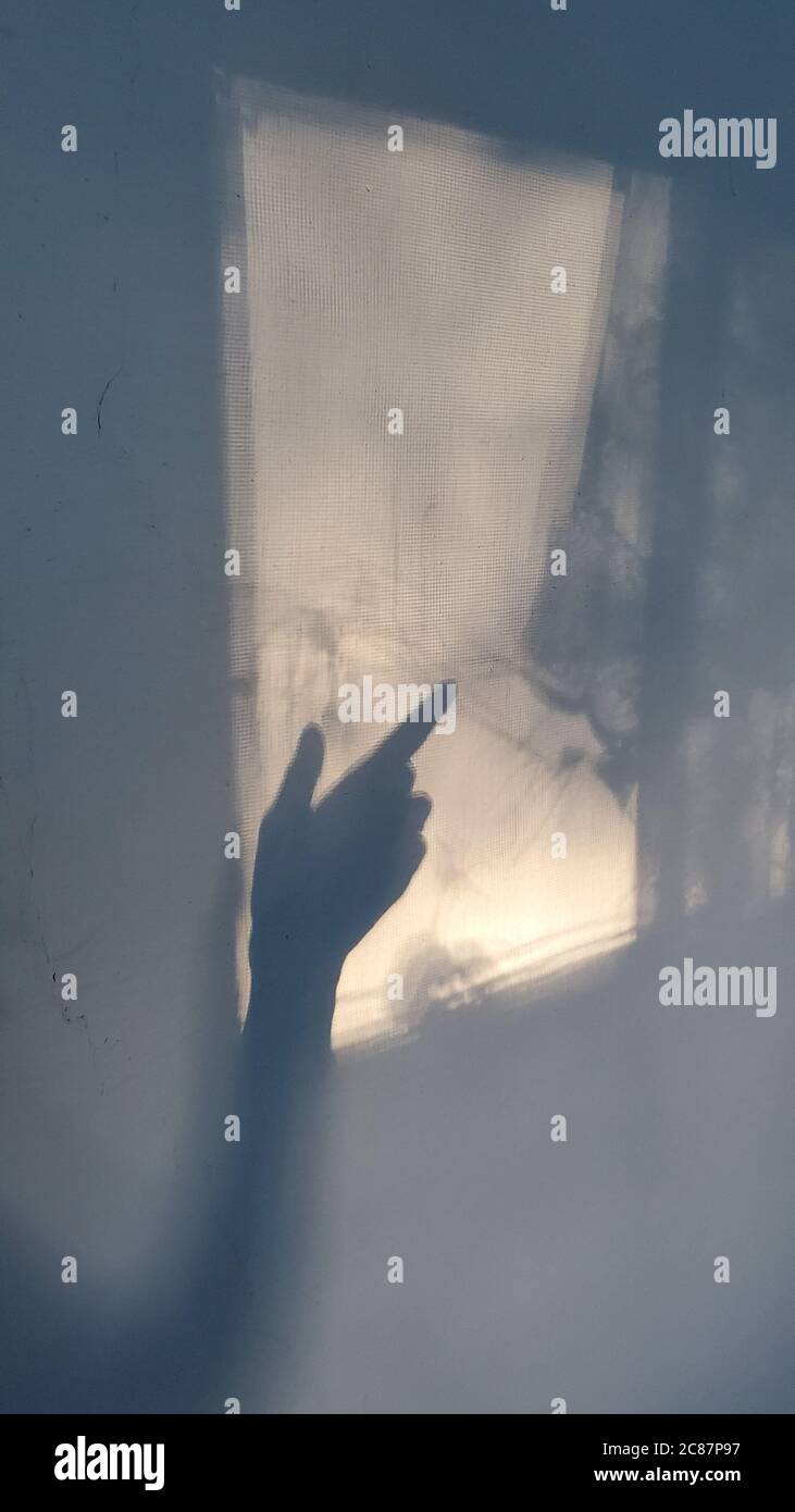 Blurry shadows of hand silhouette with forefinger poitned to window projection and looks like ghost hand gesture. Halloween concept Stock Photo