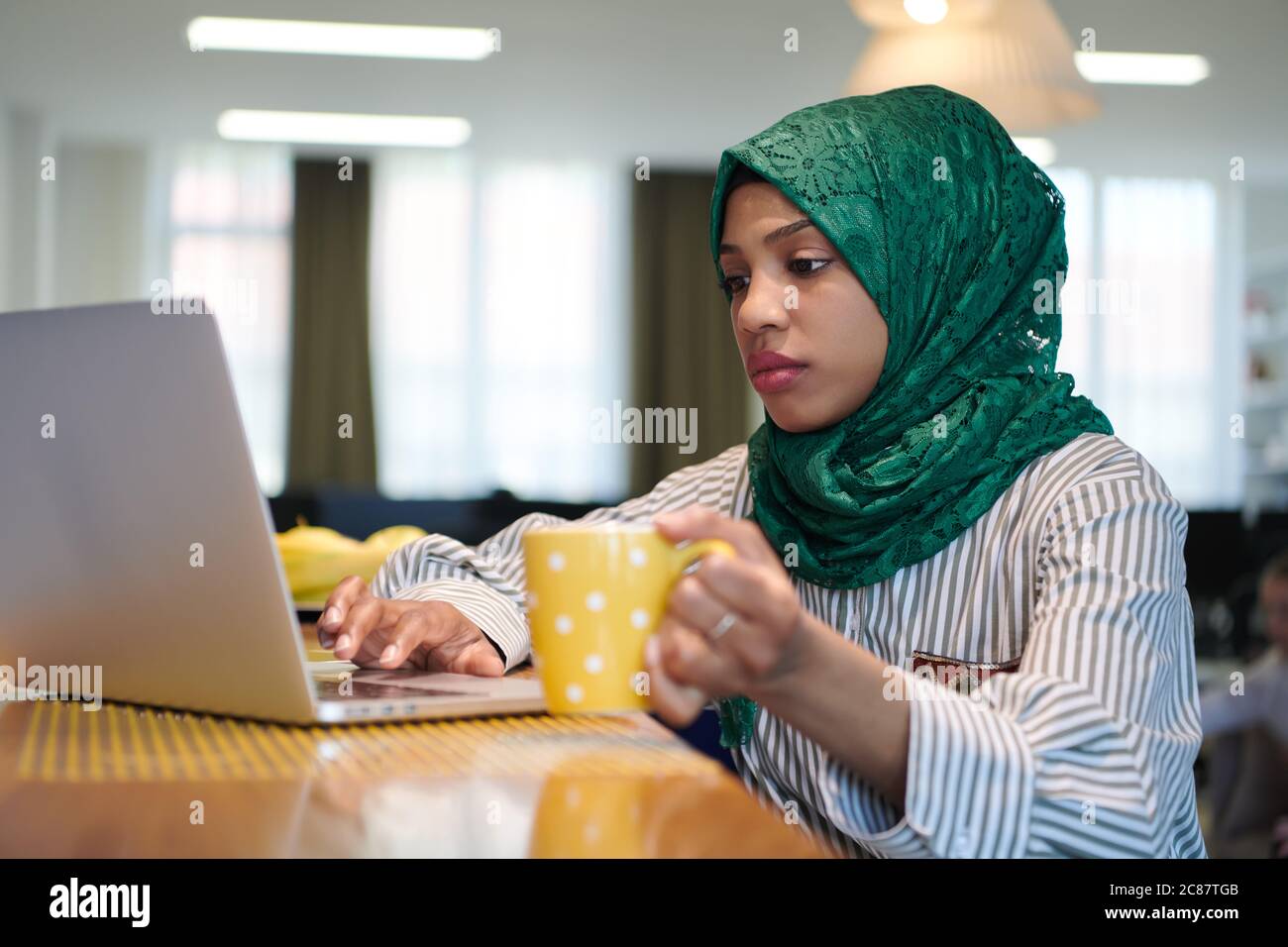 african muslim business woman wearing a green hijab drinking tea while ...