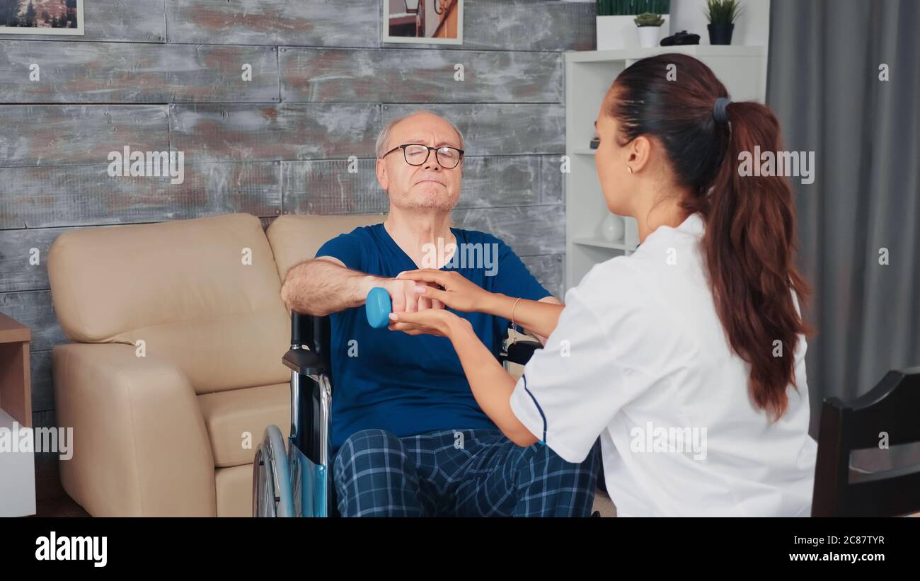 Caregiver helping senior man in wheelchair with physical thepray. Disabled handicapped old