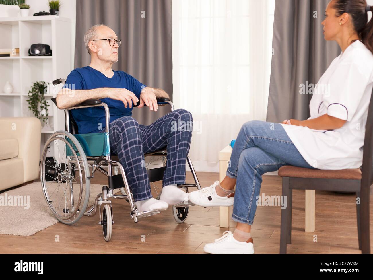 Patient and doctor talking in cozy apartment. Disabled disability old