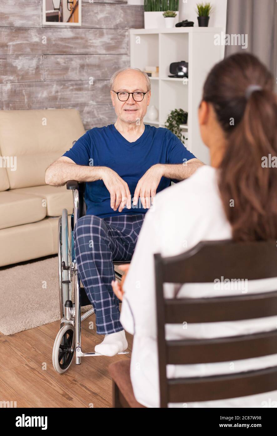 Nurse consulting an old man in wheelchair sitting in the living room. Disabled disability old person with medical worker in nursing care home assistance, healthcare and medicine service Stock Photo