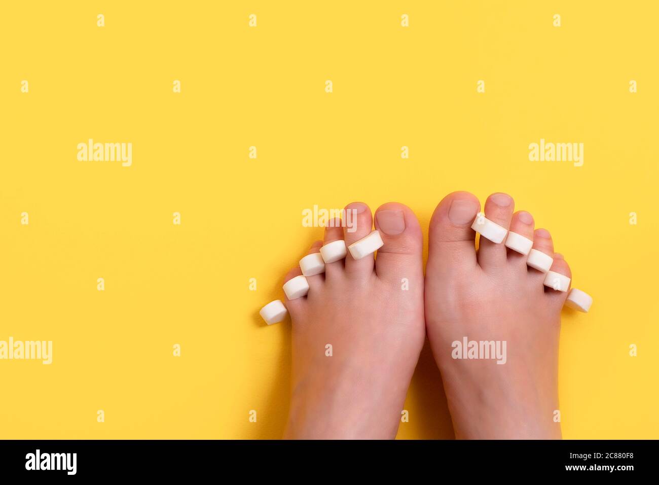 Female feet with sponge for pedicure on fingers on bright yellow background with copy space. Care about nails, pedicure and manicure beauty salon Stock Photo