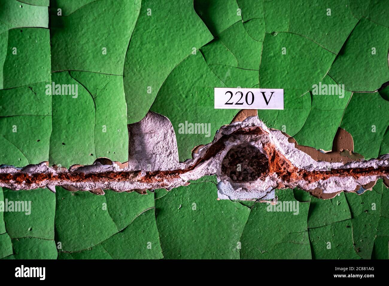 Old cracked wall with green peeling paint and empty rusty space for wiring with electricity sign, background Stock Photo