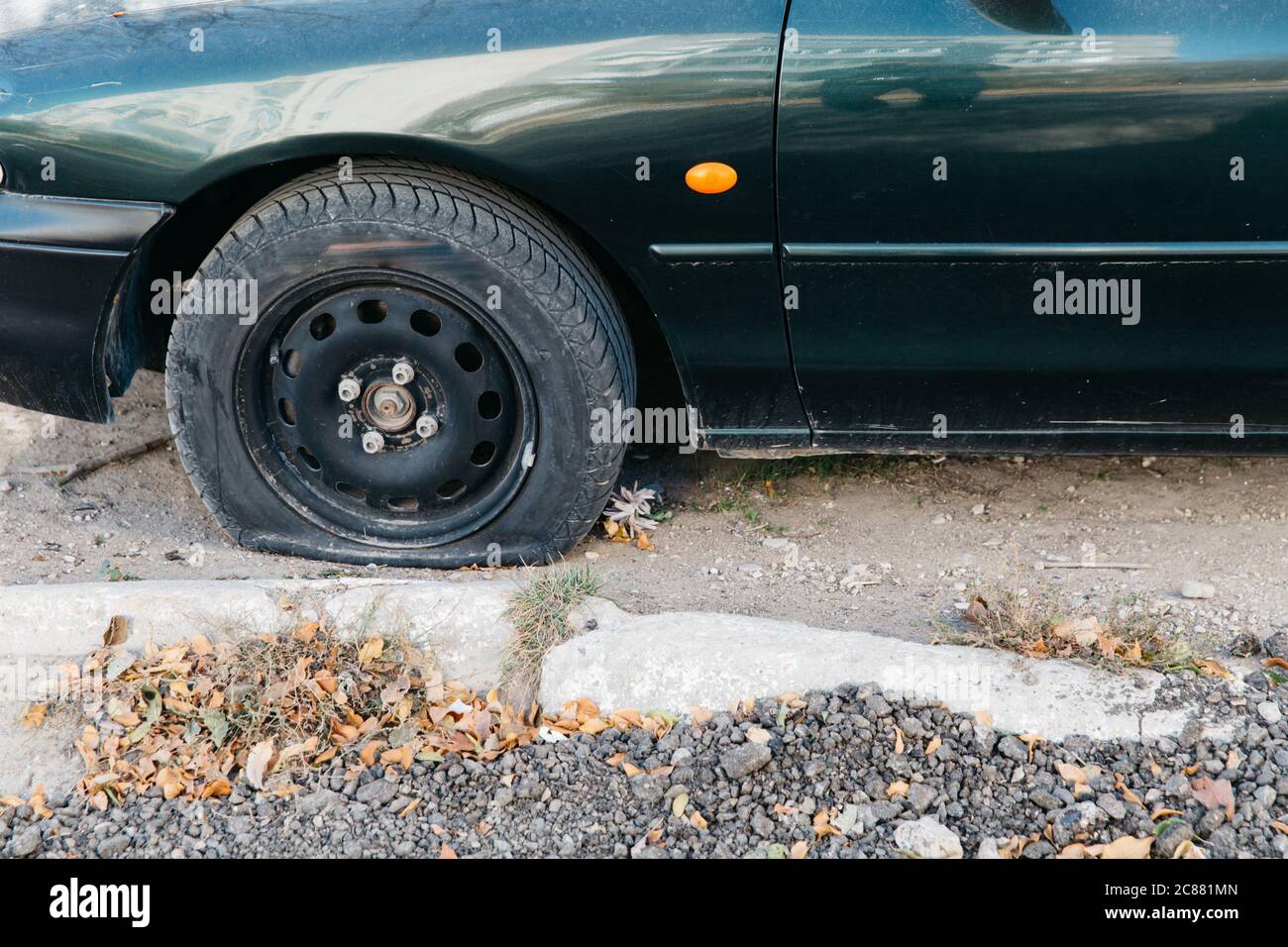 Green car with a punctured wheel in the open air. Damaged flat tire of a car. Stock Photo