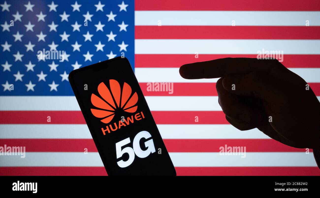 Huawei logo on smartphone silhouette and hand pointing at it. The US blurred flag on the background screen. NOT A MONTAGE, real photo. Stock Photo