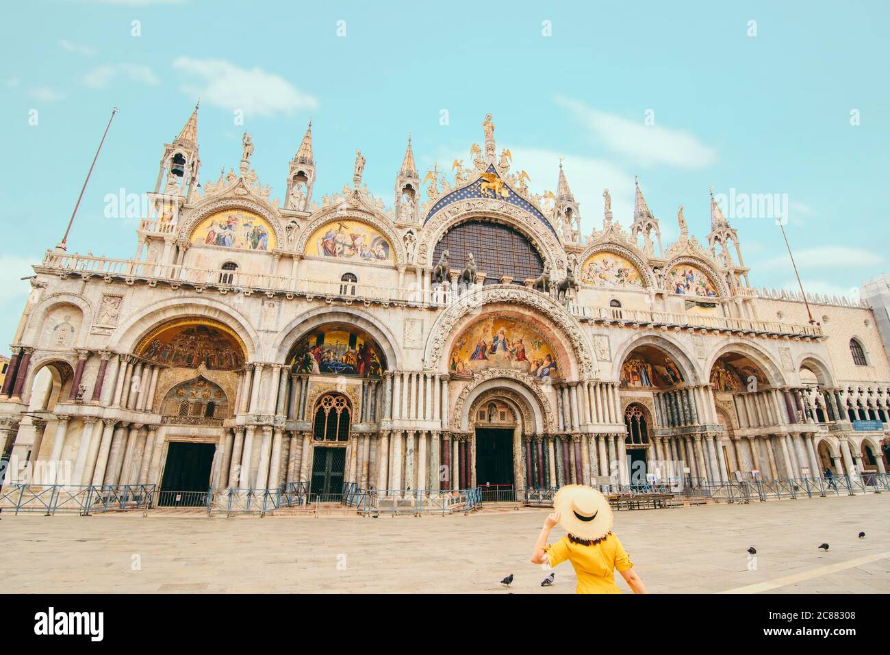 woman in yellow sundress with straw hat walking to saint mark basilica Stock Photo