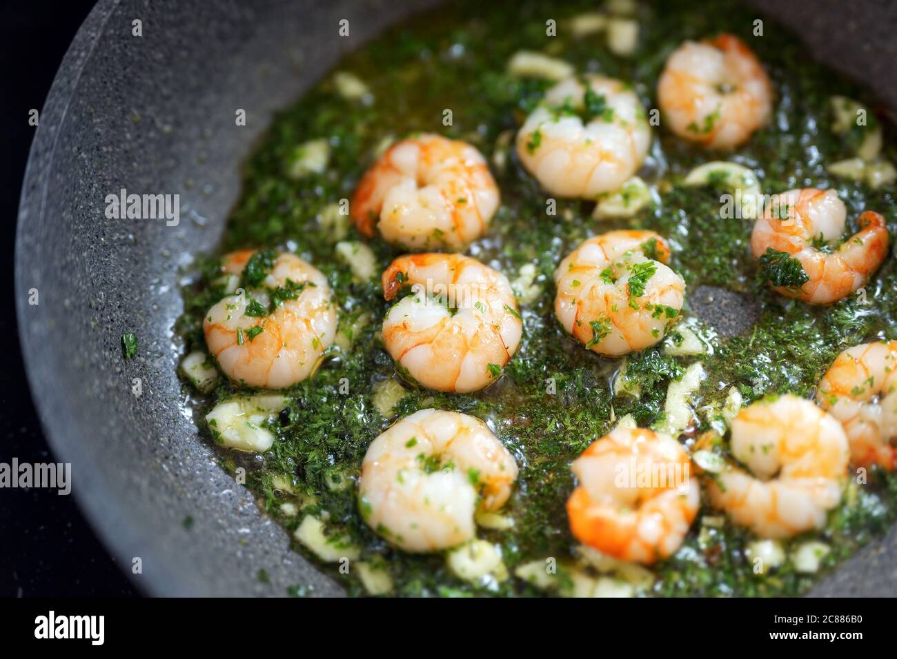 Shrimps with herbs and garlic oil are fried in a pan, cooking seafood concept, selected focus, very narrow depth of field Stock Photo