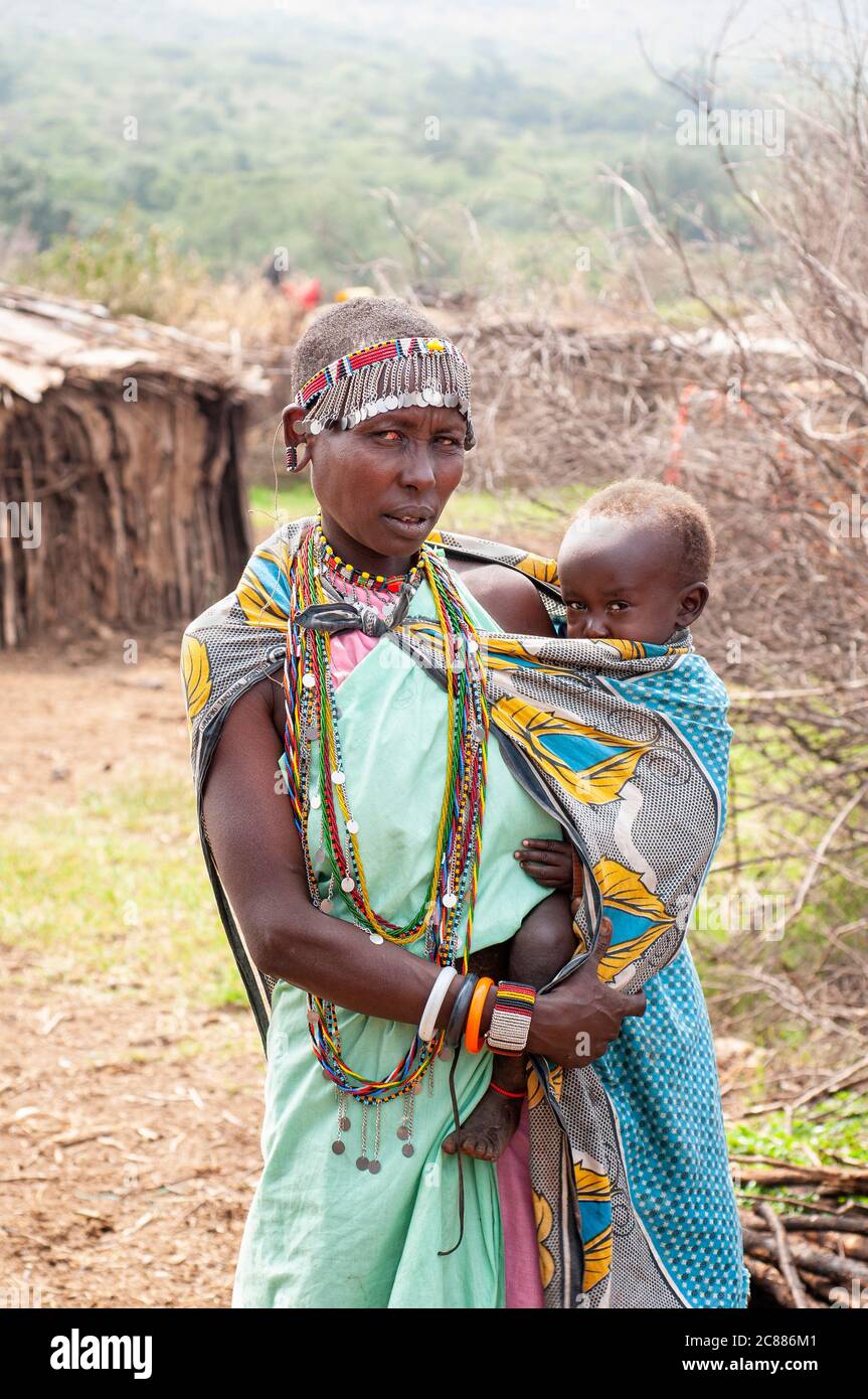 Maasai young mother and baby, wearing traditional attire, in a maasai village. Maasai Mara National Reserve. Kenya. Africa. Stock Photo