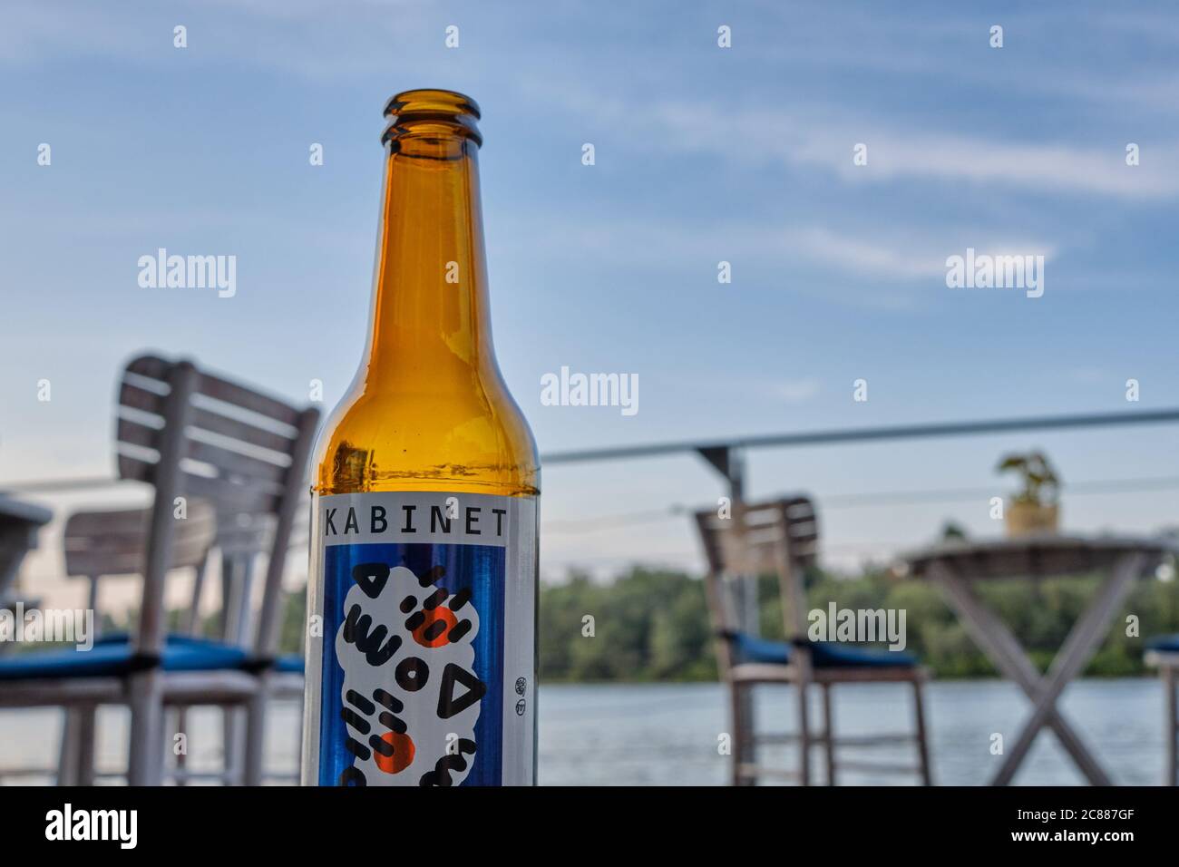 Belgrade / Serbia - August 24, 2019: Kabinet brewery craft beer bottle, with bar chairs and tables and Danube river in the background. Laid-back, easy Stock Photo
