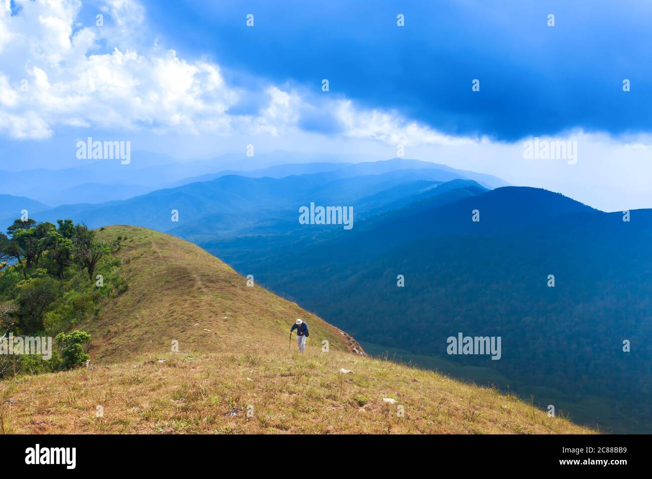 A senior man hiking with hiking pole on the peak of mountain, magical blue clouds and mountain range in the backgrounds. Stock Photo