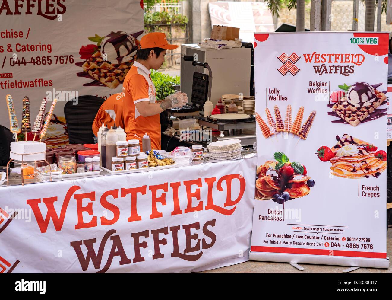 An employee working at a food stall serving waffles, crepes, and pancakes at a food festival Stock Photo