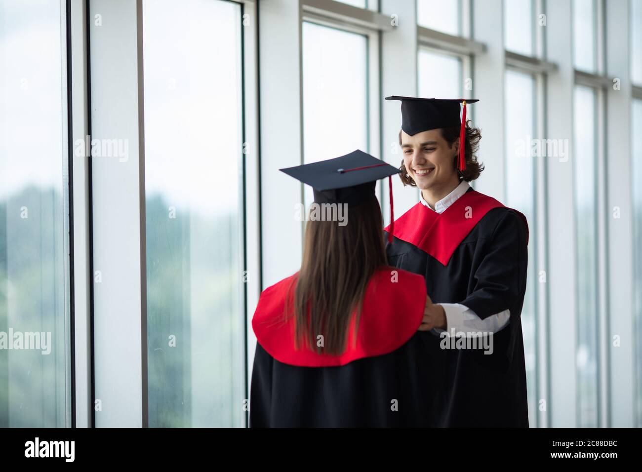 Happy international students in mortar boards and bachelor gowns greeting each other by handshake in University Stock Photo