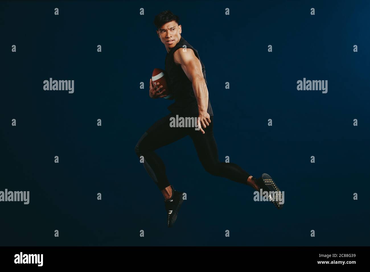 American footballer practicing tackle. Fit man in sportswear running with a football in hand. Stock Photo
