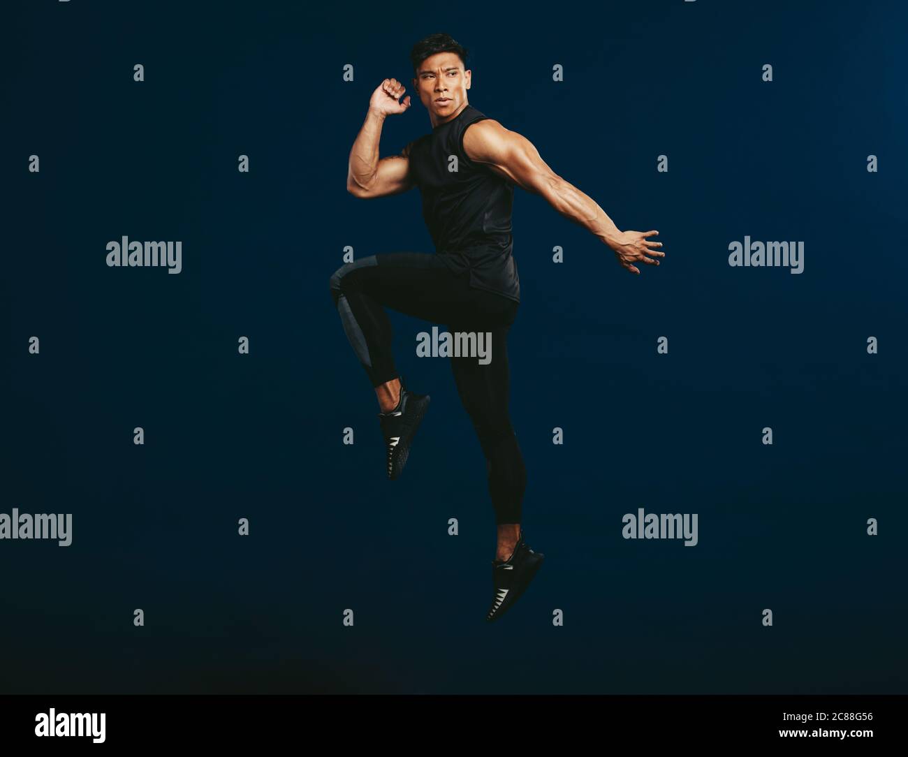 Full length of healthy male in sportswear exercising and jumping. Sportsman jumping and stretching against dark background. Stock Photo