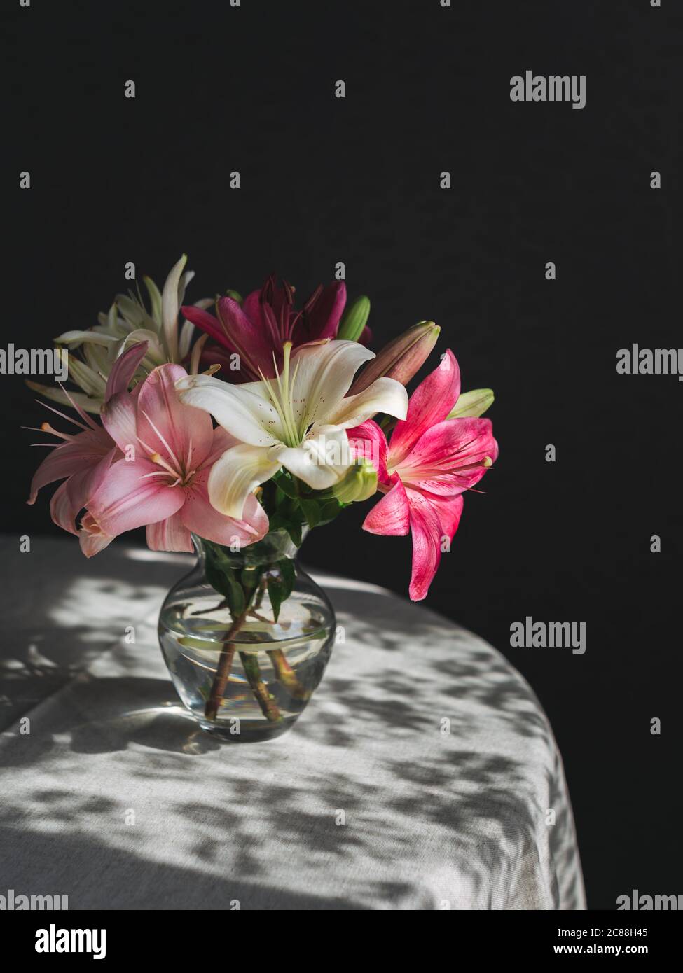 Romantic bouquet of the white and pink lilies in a glass vase on a dark ...