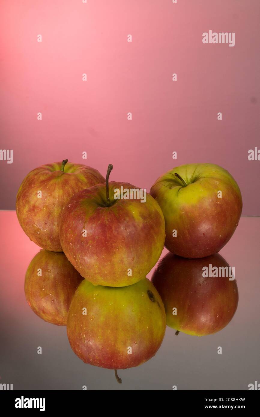 Three red apples on mirroring table on mirror red background with reflection isolated close up Stock Photo
