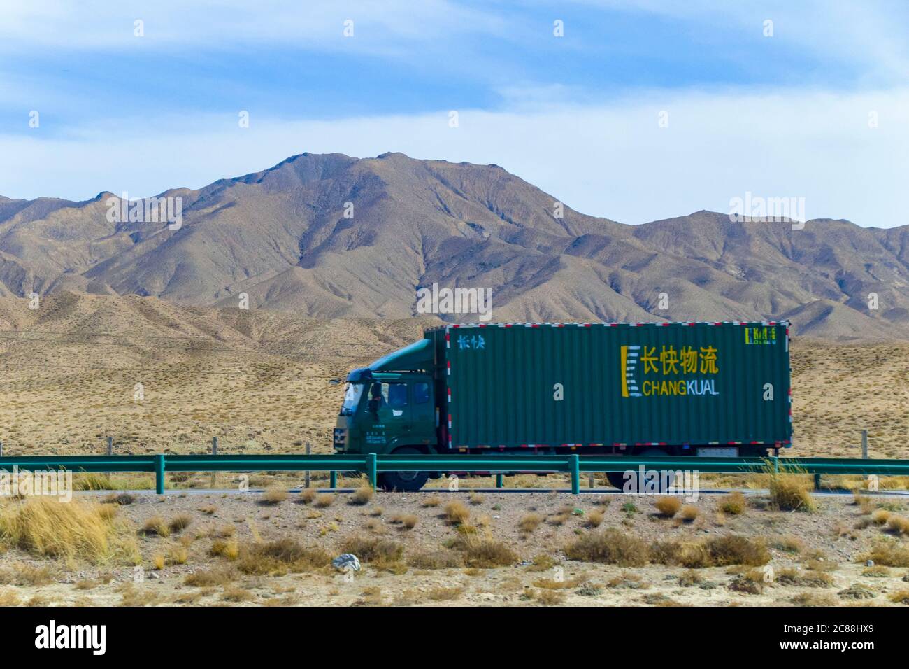 The green truck driving on Qinghai - Tibet highway. long highway on gobi desert, road has been sand blowing with wilderness background in Qingha.China Stock Photo