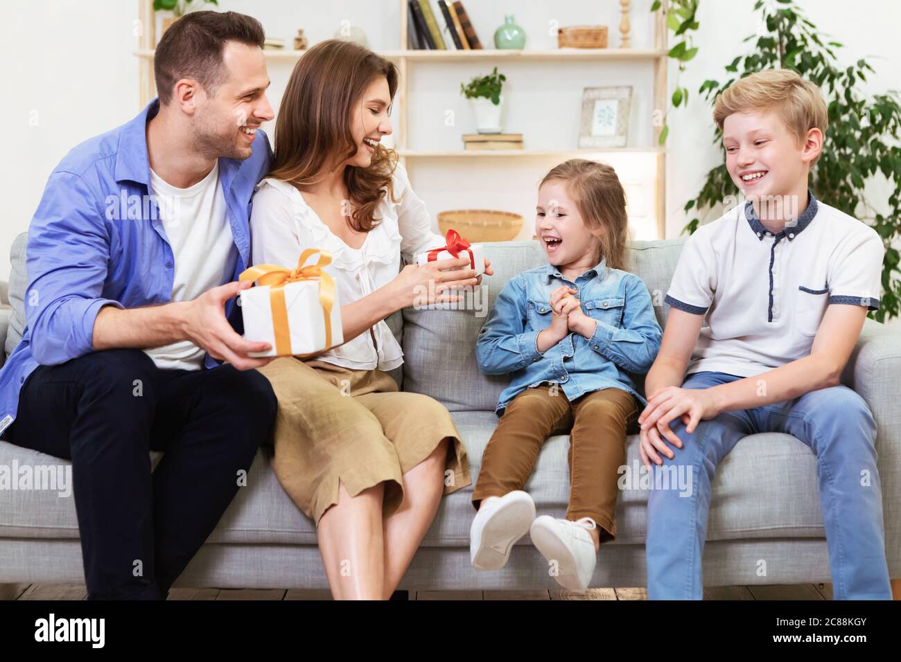 Parents Giving Gifts To Children Sitting On Sofa At Home Stock Photo